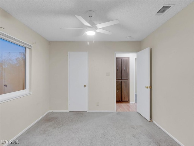 unfurnished bedroom with light carpet, ceiling fan, and a textured ceiling