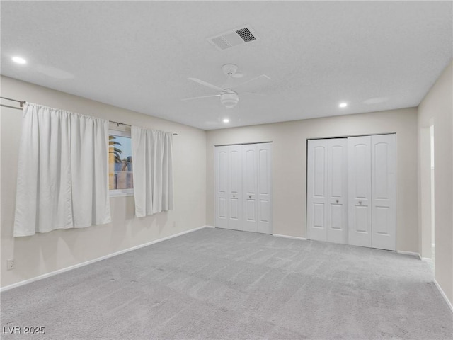 unfurnished bedroom featuring light colored carpet, two closets, and ceiling fan