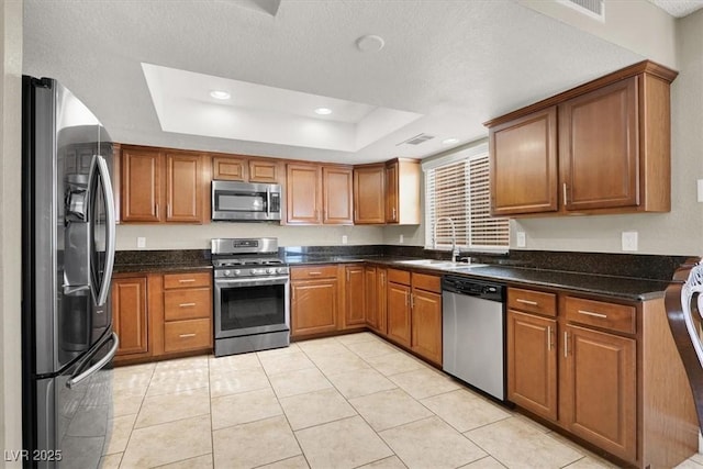 kitchen featuring dark stone countertops, sink, a tray ceiling, appliances with stainless steel finishes, and light tile patterned floors