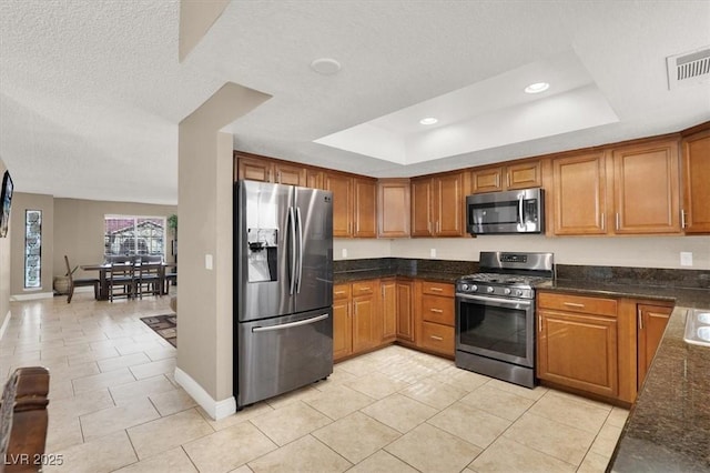 kitchen with dark stone countertops, a raised ceiling, stainless steel appliances, and light tile patterned flooring