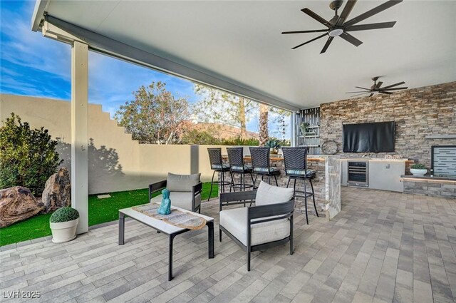 view of patio featuring an outdoor kitchen, a bar, ceiling fan, and wine cooler