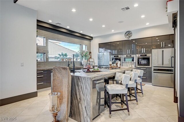 kitchen featuring a large island, light tile patterned flooring, a kitchen bar, light stone countertops, and appliances with stainless steel finishes