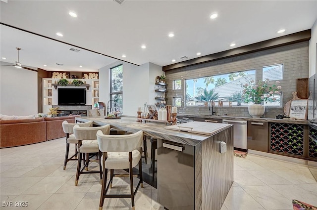 kitchen with a large island with sink, light tile patterned floors, a breakfast bar, sink, and stainless steel dishwasher