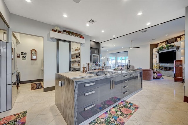 kitchen with ceiling fan, built in features, a large island with sink, gray cabinetry, and appliances with stainless steel finishes