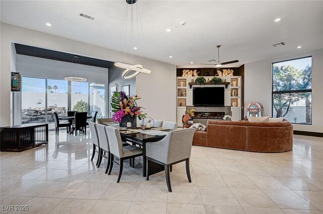 dining space with ceiling fan with notable chandelier and built in shelves