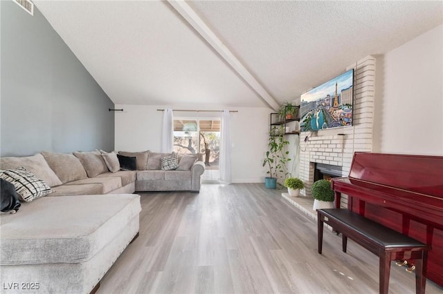 living room featuring a textured ceiling, light hardwood / wood-style flooring, a brick fireplace, and vaulted ceiling with beams