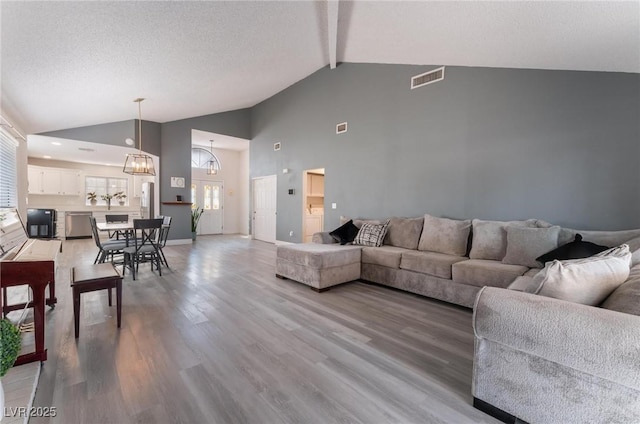 living room with a textured ceiling, hardwood / wood-style floors, high vaulted ceiling, an inviting chandelier, and beamed ceiling