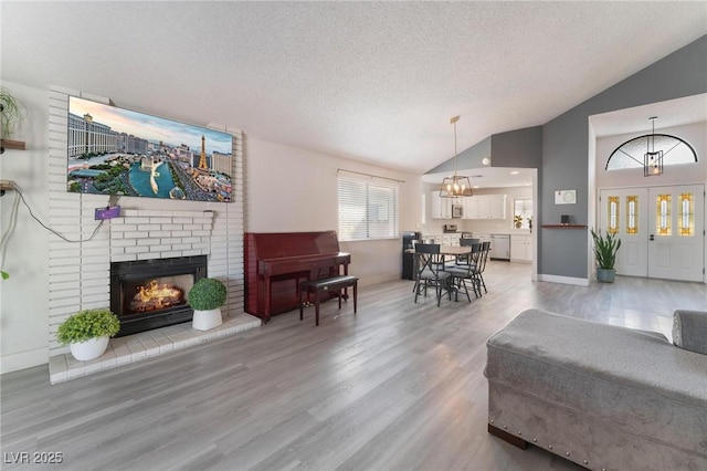 living room featuring a textured ceiling, vaulted ceiling, hardwood / wood-style flooring, a brick fireplace, and a chandelier