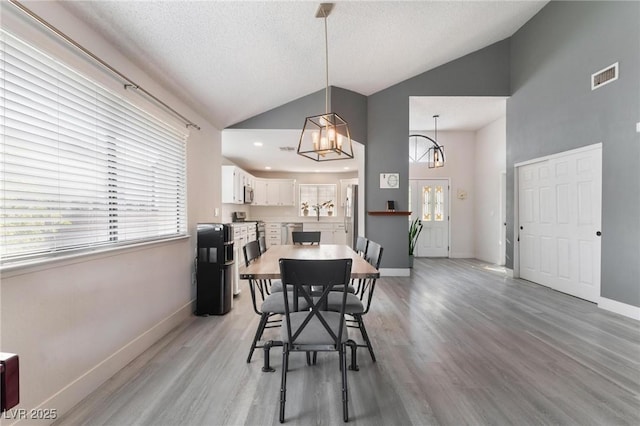 dining area featuring a textured ceiling, light wood-type flooring, an inviting chandelier, and high vaulted ceiling