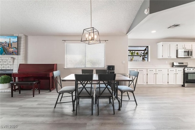 dining room featuring light hardwood / wood-style floors, an inviting chandelier, lofted ceiling, and a textured ceiling