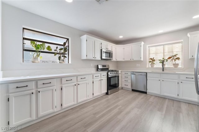 kitchen with light stone countertops, light hardwood / wood-style flooring, stainless steel appliances, white cabinetry, and sink