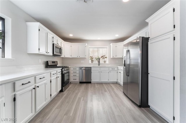 kitchen with white cabinets, stainless steel appliances, light wood-type flooring, and sink