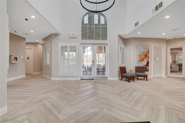 foyer entrance with light parquet flooring, french doors, and a chandelier