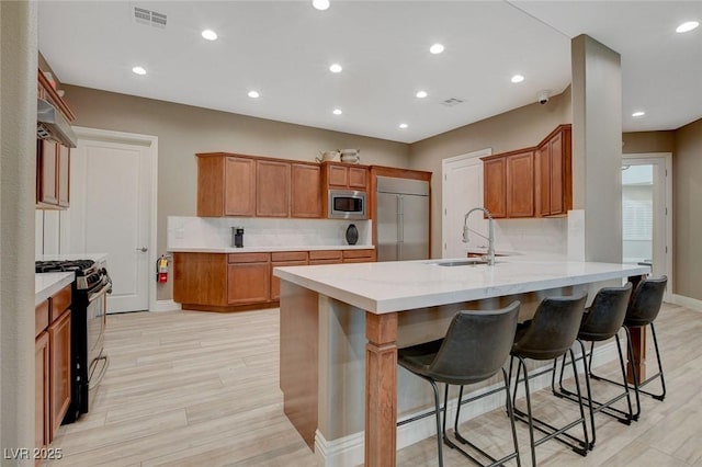 kitchen with sink, built in appliances, a kitchen bar, and light hardwood / wood-style flooring