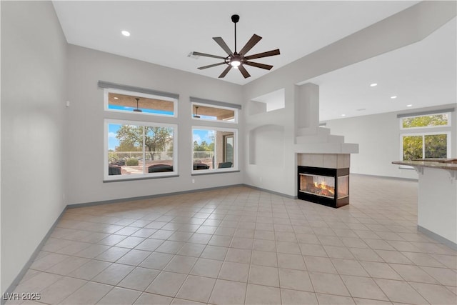 unfurnished living room with ceiling fan, light tile patterned flooring, a wealth of natural light, and a multi sided fireplace