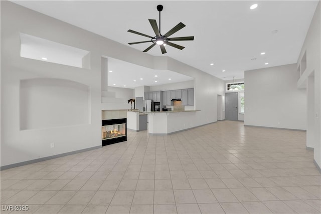 unfurnished living room with light tile patterned flooring, a tiled fireplace, ceiling fan, and a high ceiling