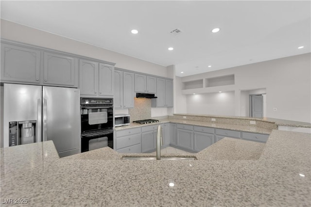 kitchen featuring light stone counters, stainless steel appliances, tasteful backsplash, gray cabinets, and sink