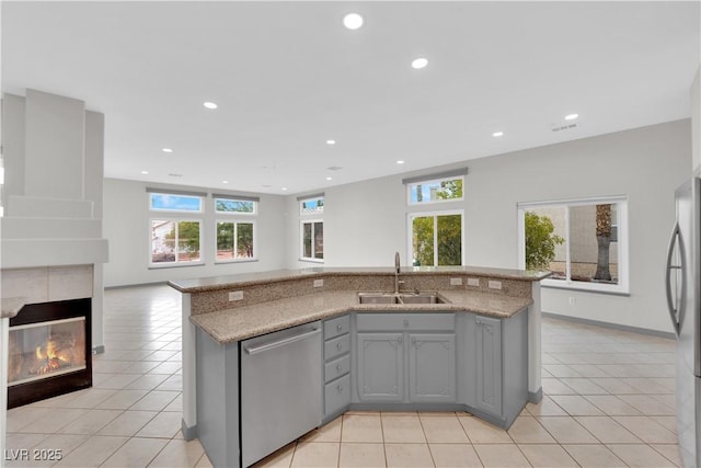 kitchen with a tile fireplace, light tile patterned floors, gray cabinetry, appliances with stainless steel finishes, and sink