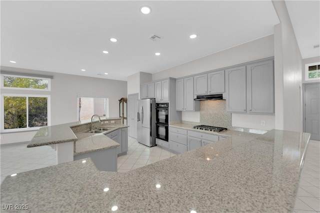 kitchen with a kitchen island with sink, gray cabinets, stainless steel appliances, light stone counters, and backsplash