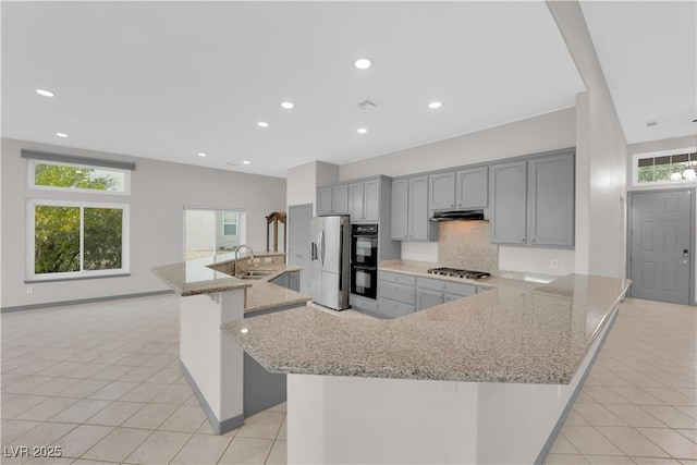 kitchen featuring a kitchen island with sink, gray cabinetry, stainless steel appliances, light stone countertops, and sink