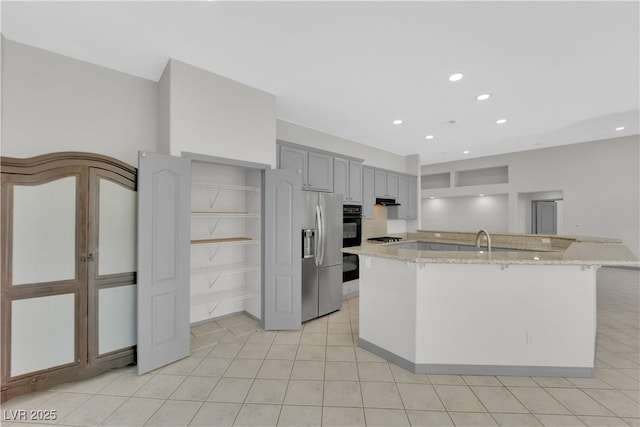 kitchen featuring light stone countertops, stainless steel fridge with ice dispenser, gray cabinets, a kitchen island with sink, and sink