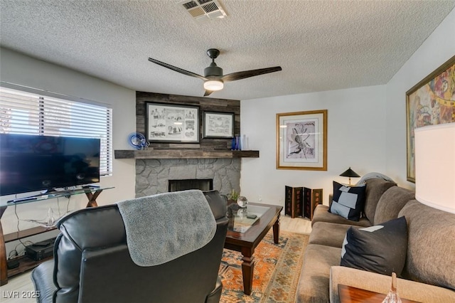 living room featuring a fireplace, ceiling fan, and a textured ceiling