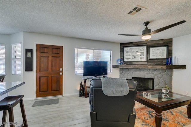 living room with a textured ceiling, ceiling fan, and a stone fireplace