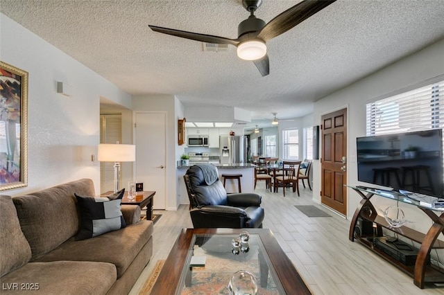 living room featuring light hardwood / wood-style floors, ceiling fan, and a textured ceiling