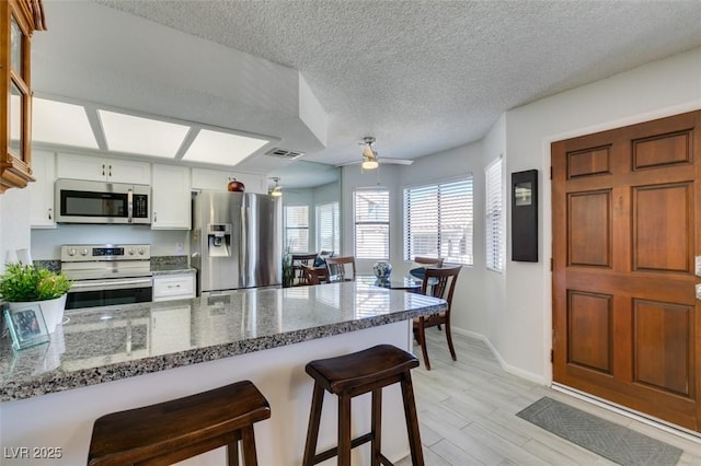 kitchen with a textured ceiling, stainless steel appliances, white cabinetry, ceiling fan, and a kitchen breakfast bar