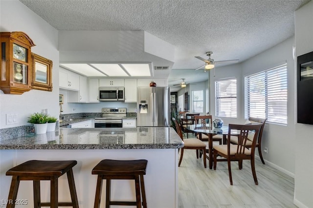 kitchen with stainless steel appliances, white cabinets, a textured ceiling, and kitchen peninsula