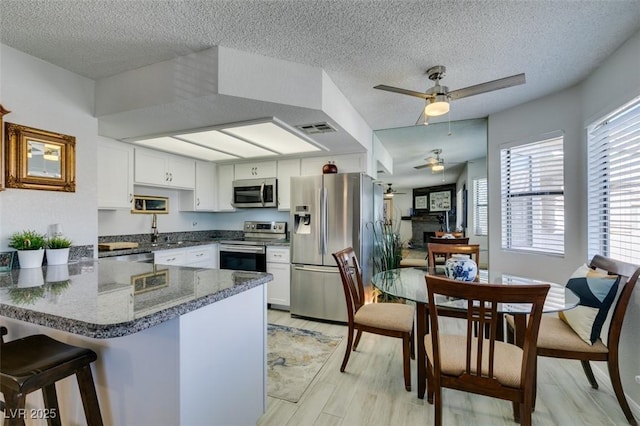 kitchen featuring appliances with stainless steel finishes, kitchen peninsula, ceiling fan, a textured ceiling, and white cabinets