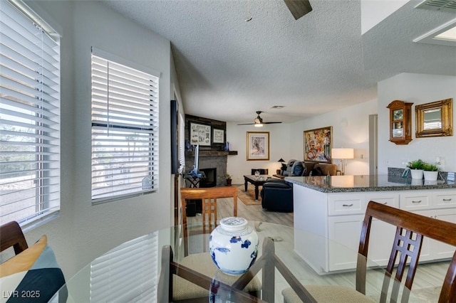 dining area with ceiling fan, light wood-type flooring, a textured ceiling, and a large fireplace