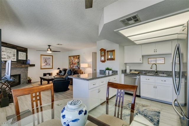 kitchen featuring appliances with stainless steel finishes, white cabinets, a stone fireplace, and sink