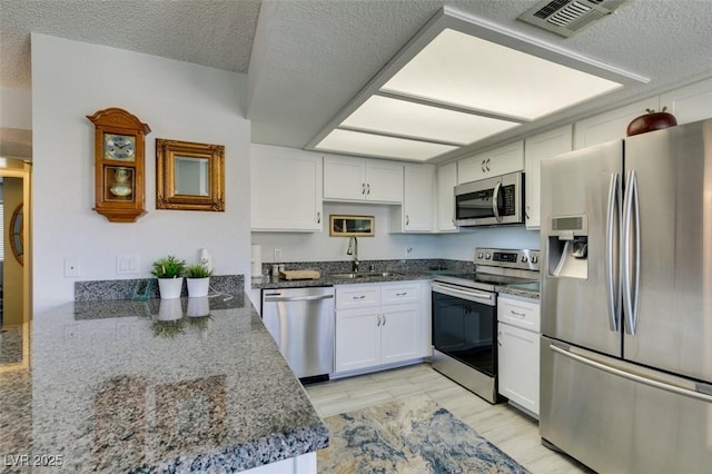 kitchen with stainless steel appliances, sink, white cabinetry, dark stone countertops, and kitchen peninsula