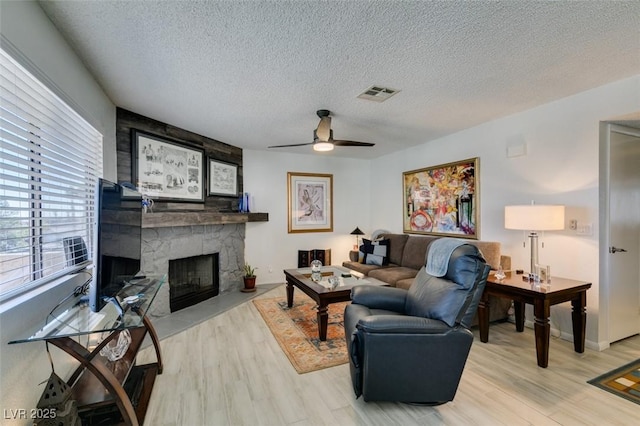 living room with a fireplace, a textured ceiling, ceiling fan, and light hardwood / wood-style floors