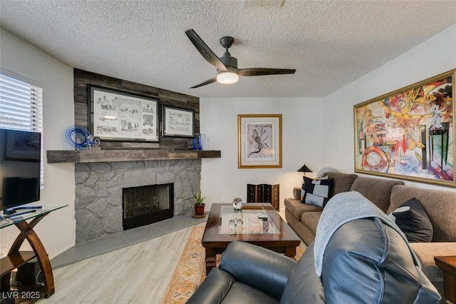 living room featuring a textured ceiling, light wood-type flooring, ceiling fan, and a fireplace