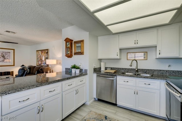 kitchen with a textured ceiling, white cabinets, dark stone counters, appliances with stainless steel finishes, and sink