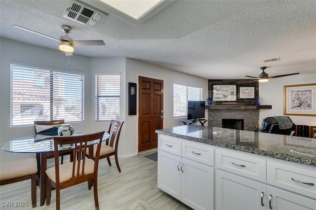 kitchen featuring dark stone counters, ceiling fan, white cabinetry, and a fireplace