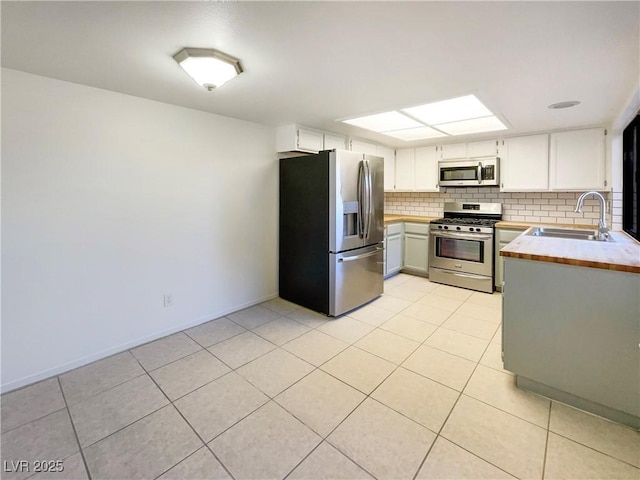 kitchen featuring appliances with stainless steel finishes, white cabinetry, sink, backsplash, and light tile patterned flooring