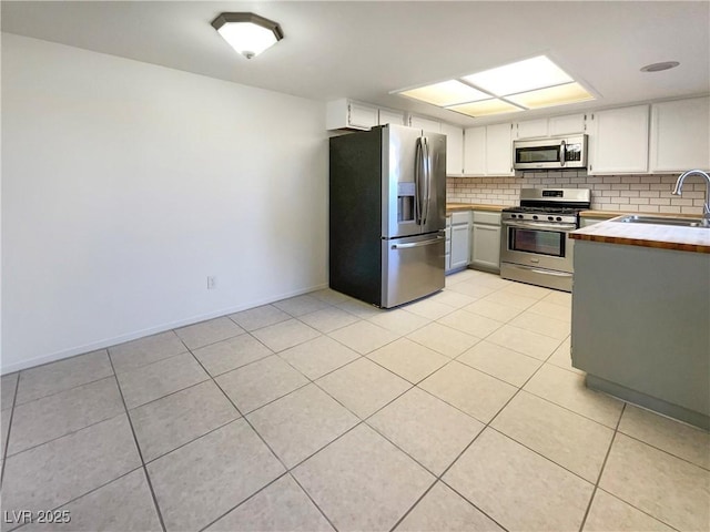 kitchen with stainless steel appliances, backsplash, light tile patterned flooring, white cabinets, and sink