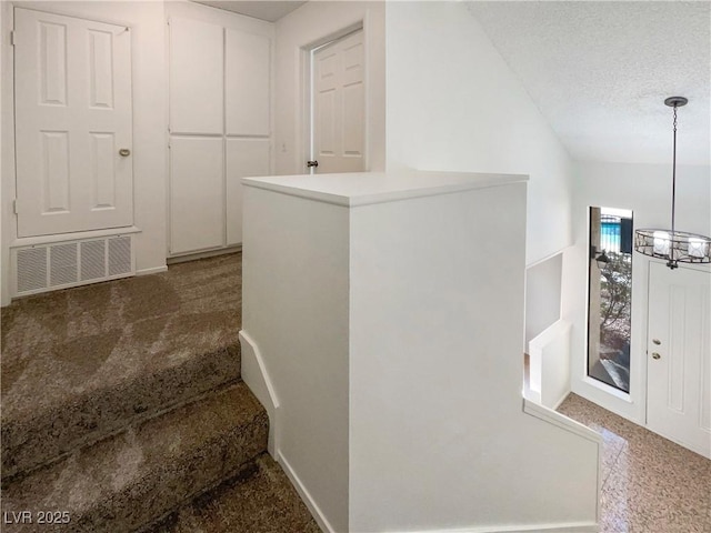 stairs featuring a notable chandelier, a textured ceiling, and carpet flooring