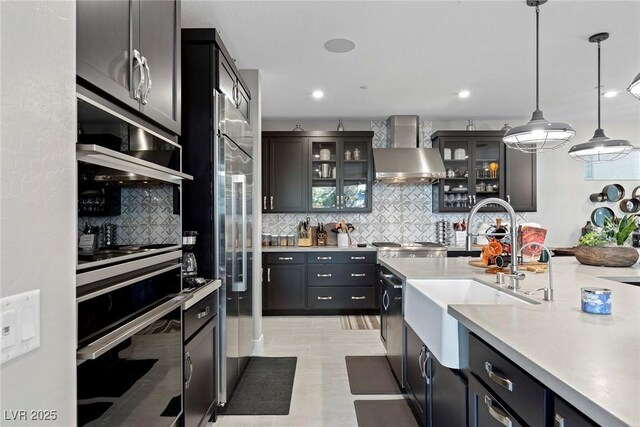 kitchen featuring appliances with stainless steel finishes, pendant lighting, sink, wall chimney range hood, and tasteful backsplash