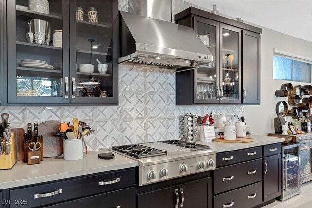 kitchen featuring stainless steel gas stovetop, wall chimney range hood, decorative backsplash, and wine cooler