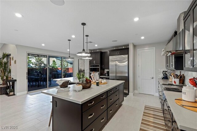 kitchen featuring hanging light fixtures, premium appliances, an island with sink, decorative backsplash, and a breakfast bar area