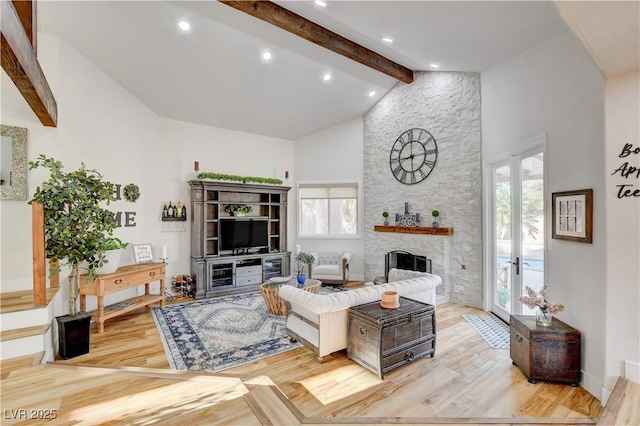 living room featuring light wood-type flooring, a stone fireplace, high vaulted ceiling, and beamed ceiling