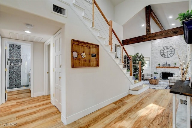 stairs with hardwood / wood-style flooring, beamed ceiling, and a stone fireplace