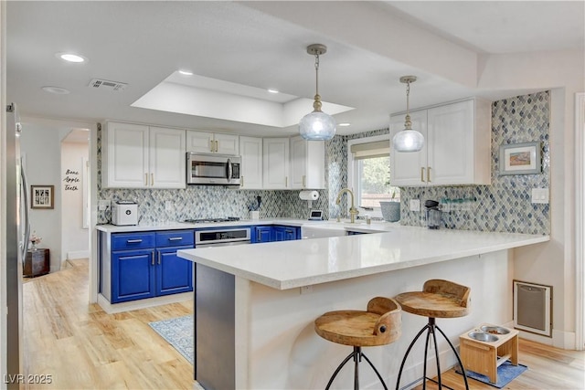 kitchen featuring decorative light fixtures, white cabinetry, blue cabinetry, a breakfast bar, and appliances with stainless steel finishes