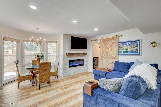 living room with washer / clothes dryer, wood-type flooring, a barn door, a chandelier, and a stone fireplace