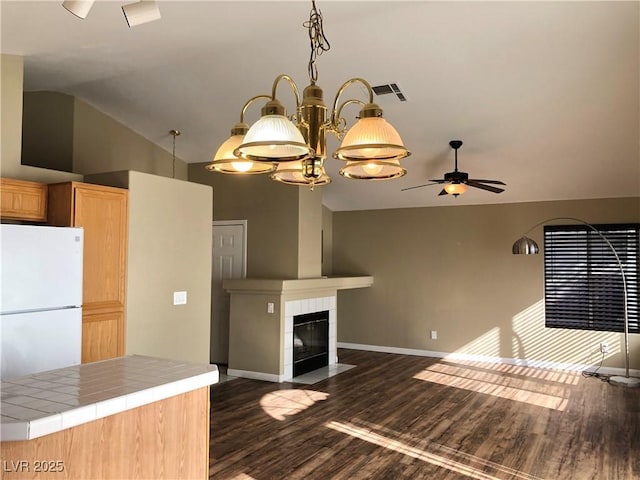 kitchen featuring tile counters, white refrigerator, a fireplace, lofted ceiling, and ceiling fan with notable chandelier