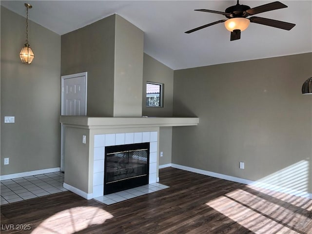 unfurnished living room featuring lofted ceiling, hardwood / wood-style flooring, a tiled fireplace, and ceiling fan